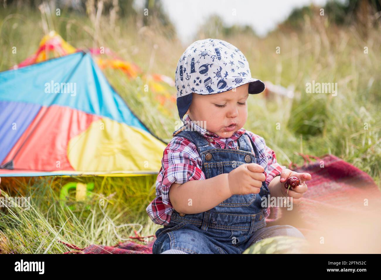 Little boy with cherry sitting on picnic blanket in the countryside