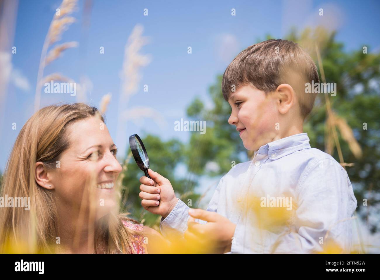 Little boy looking at his mother face with a magnifying glass in the countryside, Bavaria, Germany Stock Photo