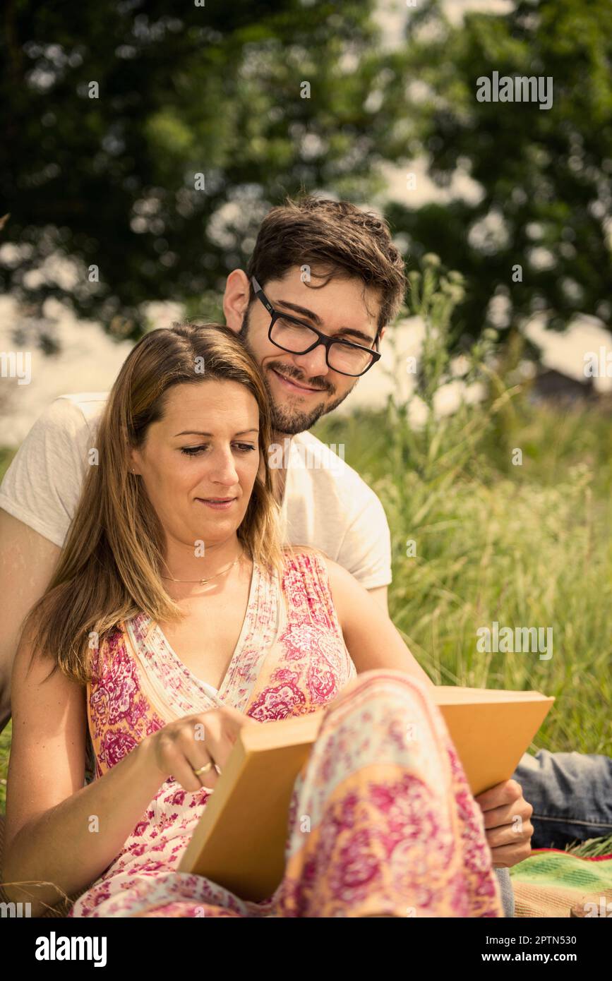 Woman with her husband and reading book on meadow in the countryside, Bavaria, Germany Stock Photo