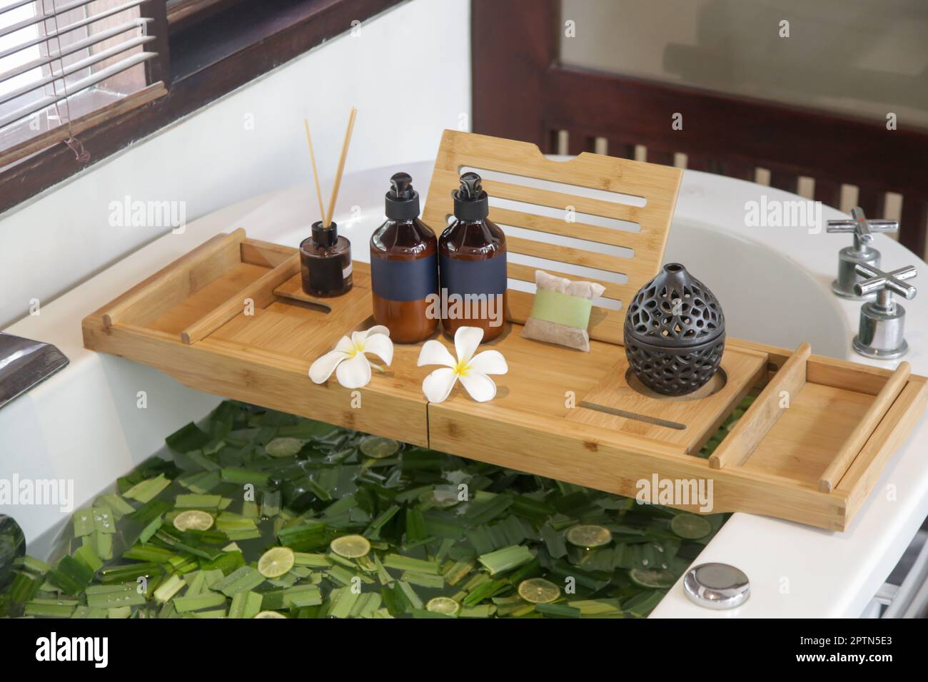 Tub full of water and herbs with wooden bathtub tray with various