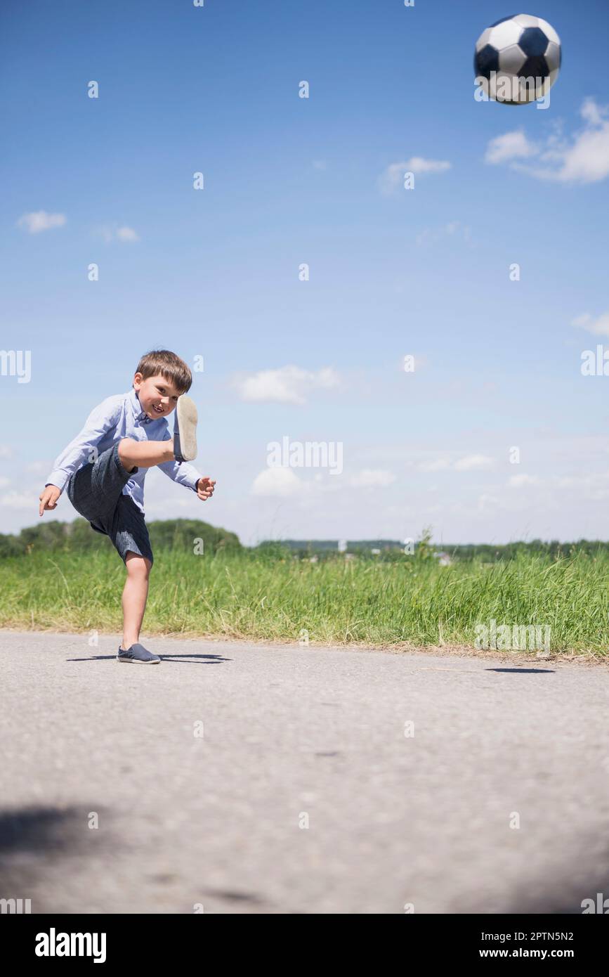 Small boy playing football on road in the countryside, Bavaria, Germany Stock Photo