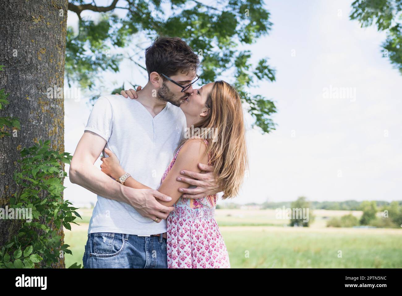 Mid adult couple kissing at each other in front of tree in the countryside, Bavaria, Germany Stock Photo