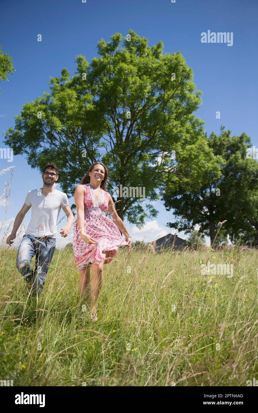 Mid adult couple running through grass on meadow in the countryside, Bavaria, Germany Stock Photo