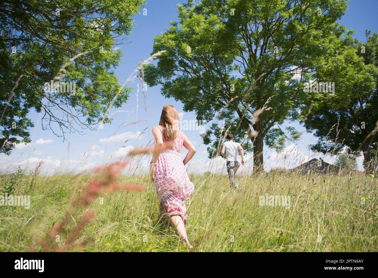 Rear view of mid adult couple running through grass on meadow in the countryside, Bavaria, Germany Stock Photo