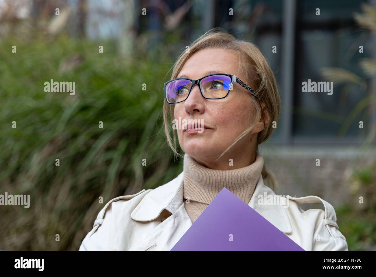 Beautiful matur woman stands near glass building with a folder Stock Photo
