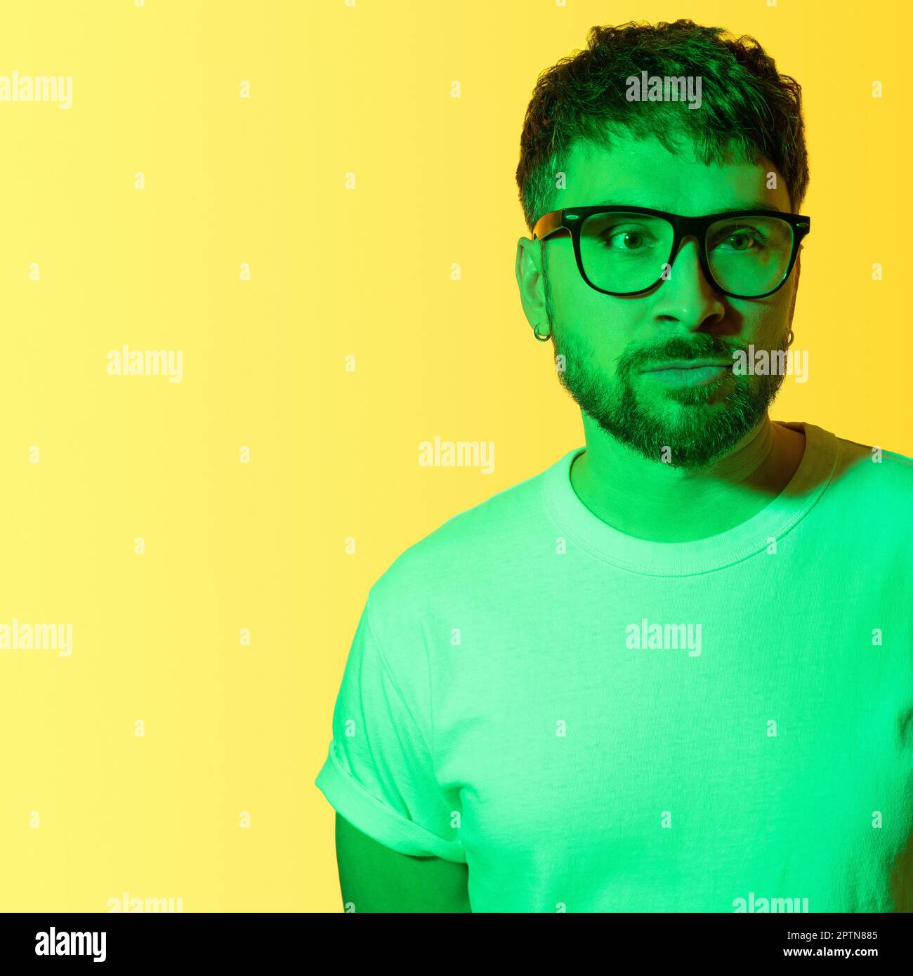 Creative portrait of a bearded middle-aged man with black framed glasses. Depressed man with mental problems sadly looking away. Colored green light Stock Photo