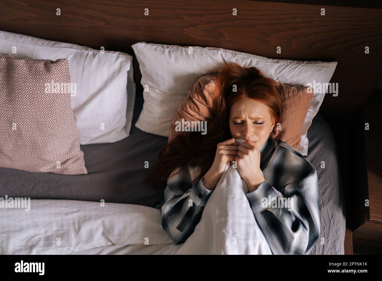 Top view portrait of sad depressed young woman crying hiding under