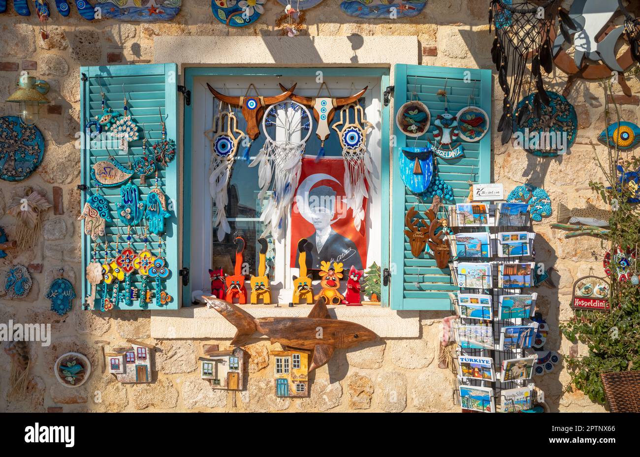 A shop decorates its stone wall and blue shuttered window with tourist souvenirs, Nazar Boncuk and trinkets as well as a poster of the founder of mode Stock Photo