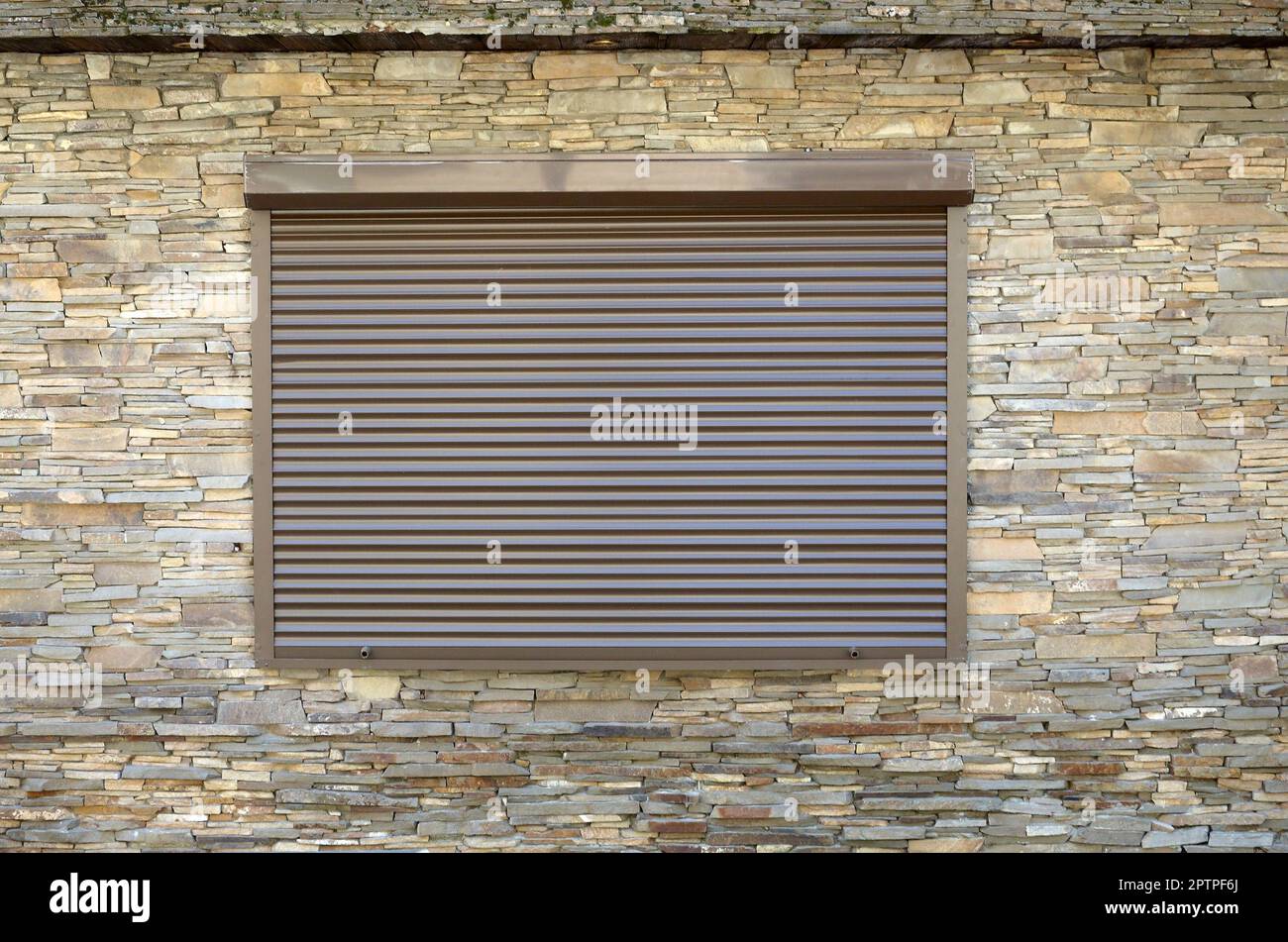 A window with brown metal rolling shutters. Wall decoration with