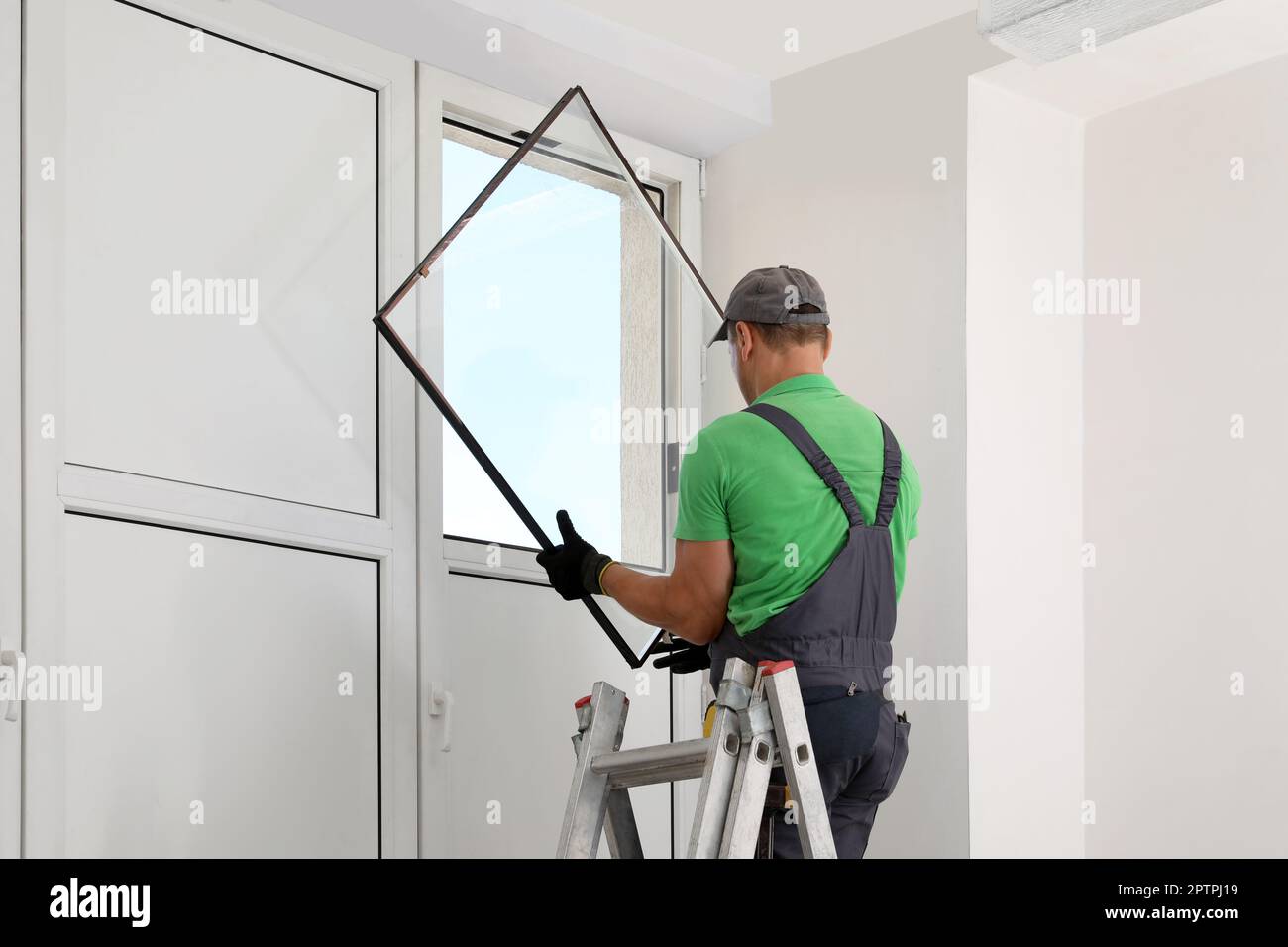 Worker on folding ladder installing window indoors Stock Photo