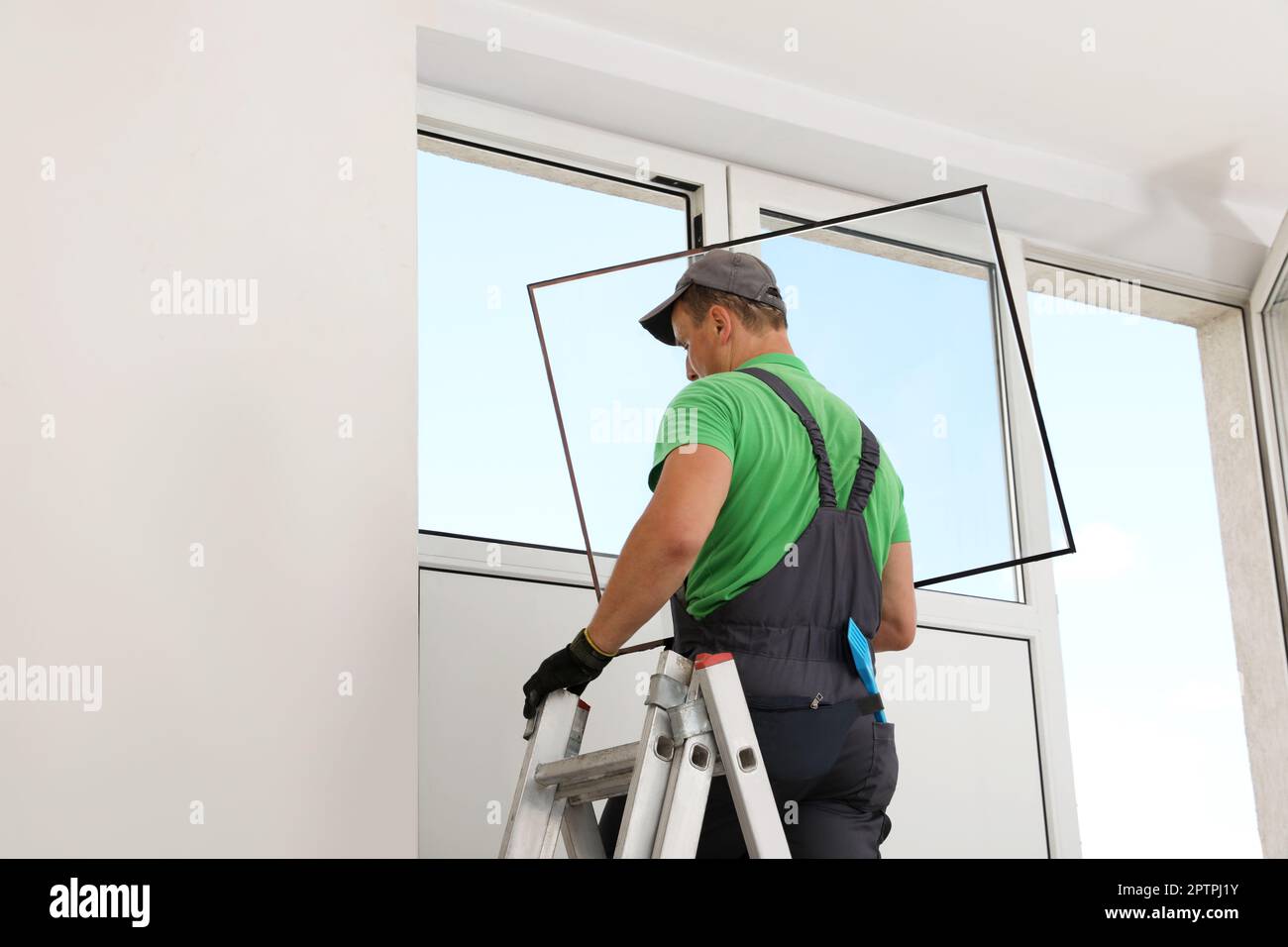 Worker on folding ladder installing window indoors Stock Photo