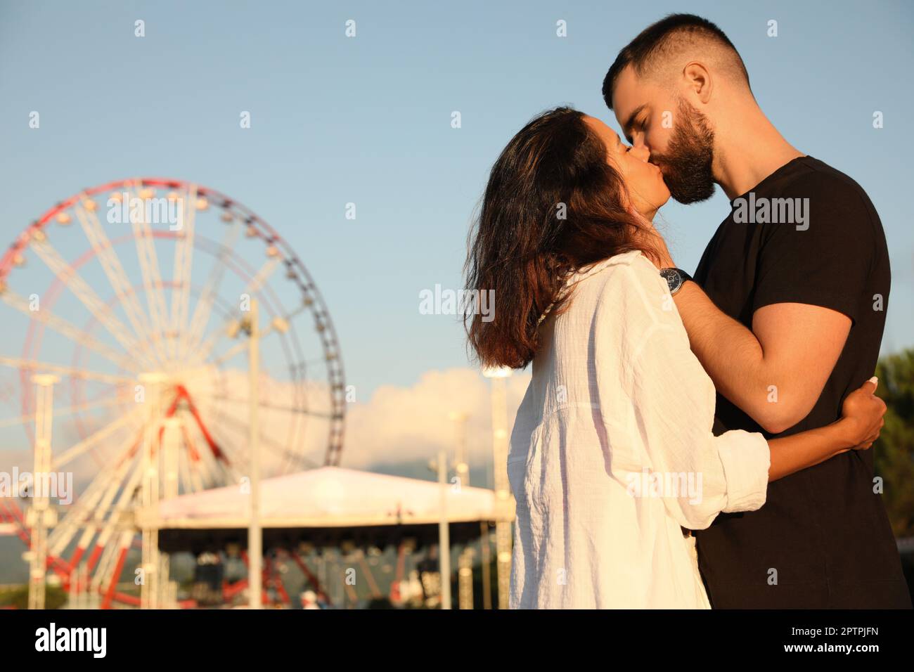 Happy young couple kissing in amusement park Stock Photo - Alamy