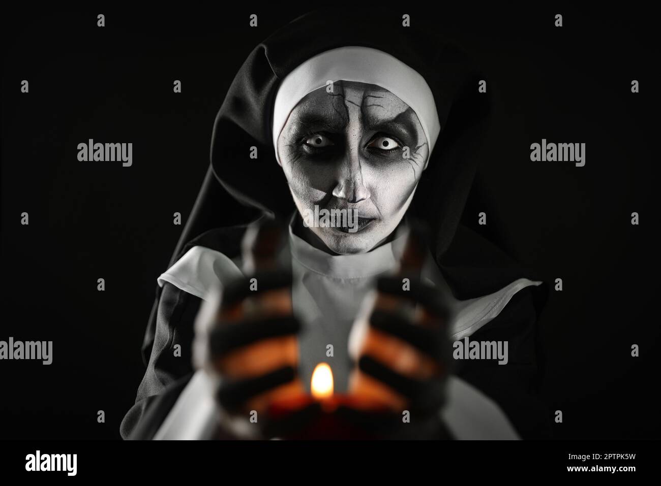 Scary devilish nun with burning candle on black background
