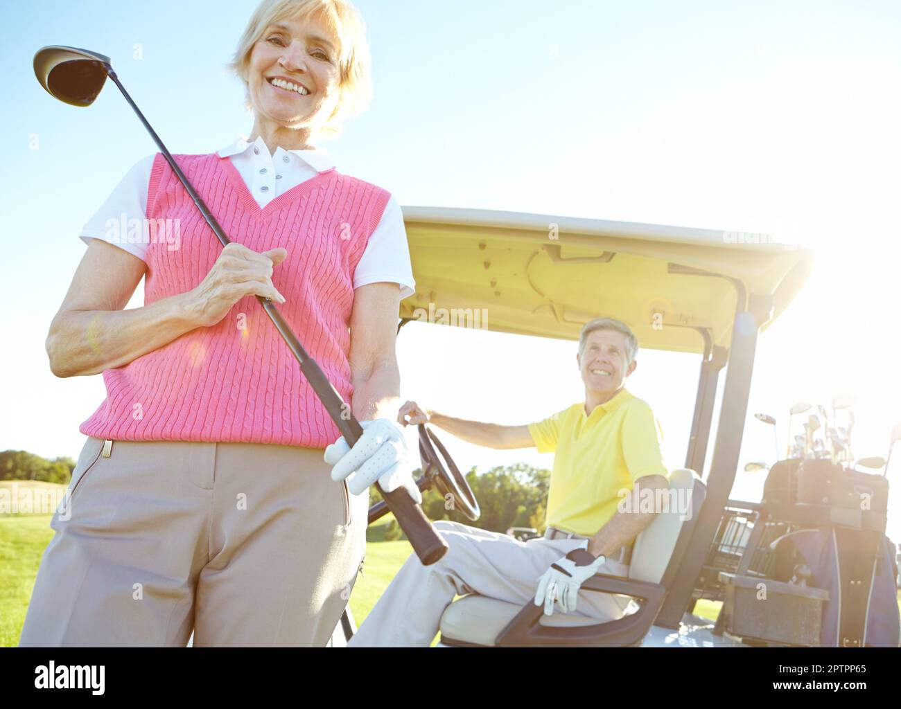 Golfing is her favorite pastime. Low angle shot of an attractive older female golfer standing in front of a golf cart with her golfing buddy behind Stock Photo