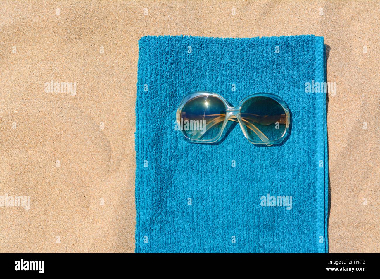 Soft blue beach towel with sunglasses on sand, top view. Space for text ...
