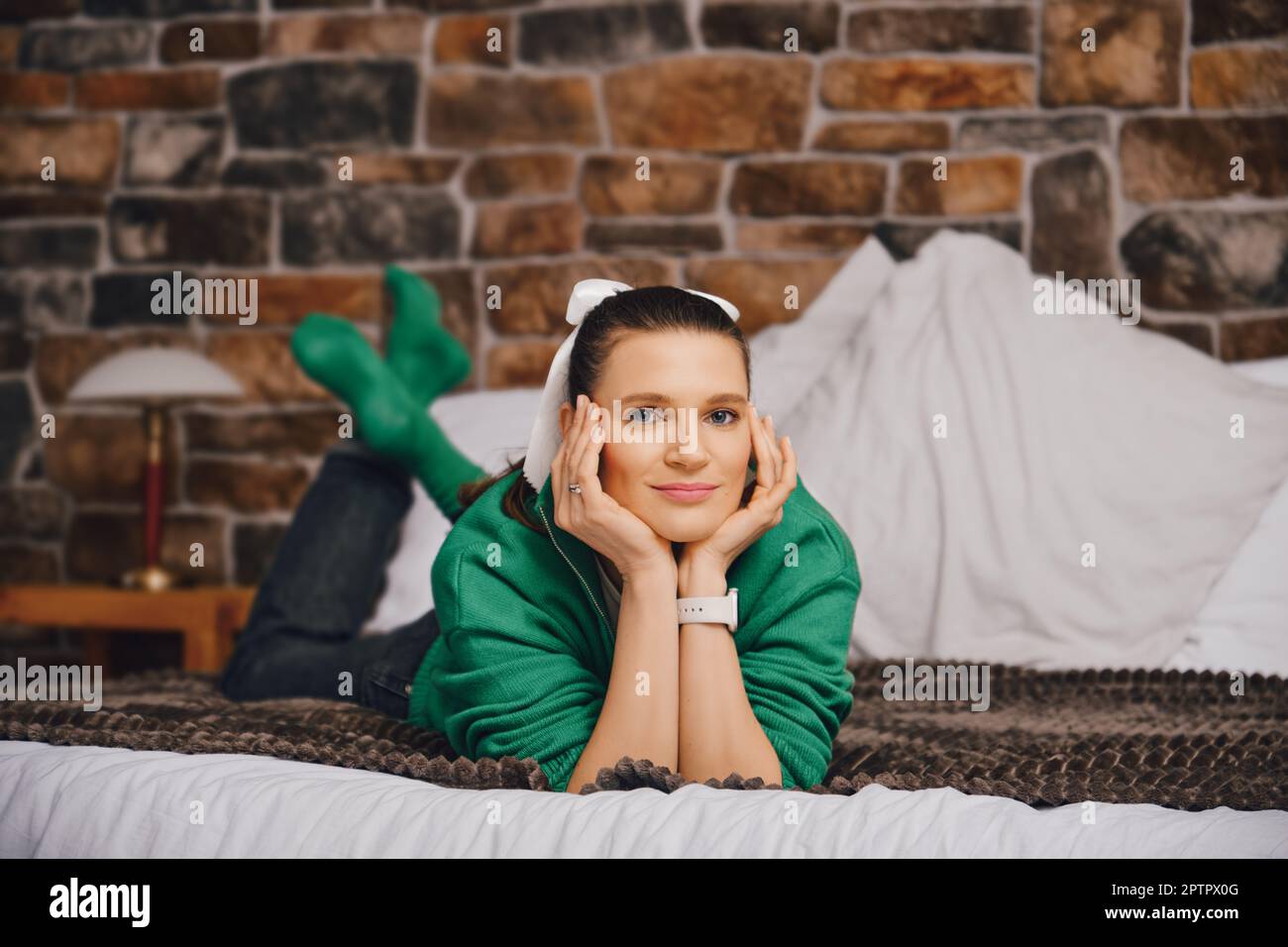 Pensive and positive woman lying on bed in her bedroom propping her