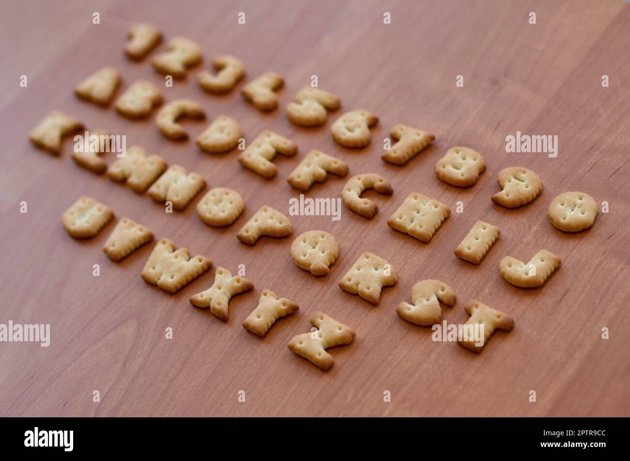 Letters of salty crackers lay on a wooden brown surface in the order similar to the layout of the English alphabet. Funny imitation of the school alph Stock Photo