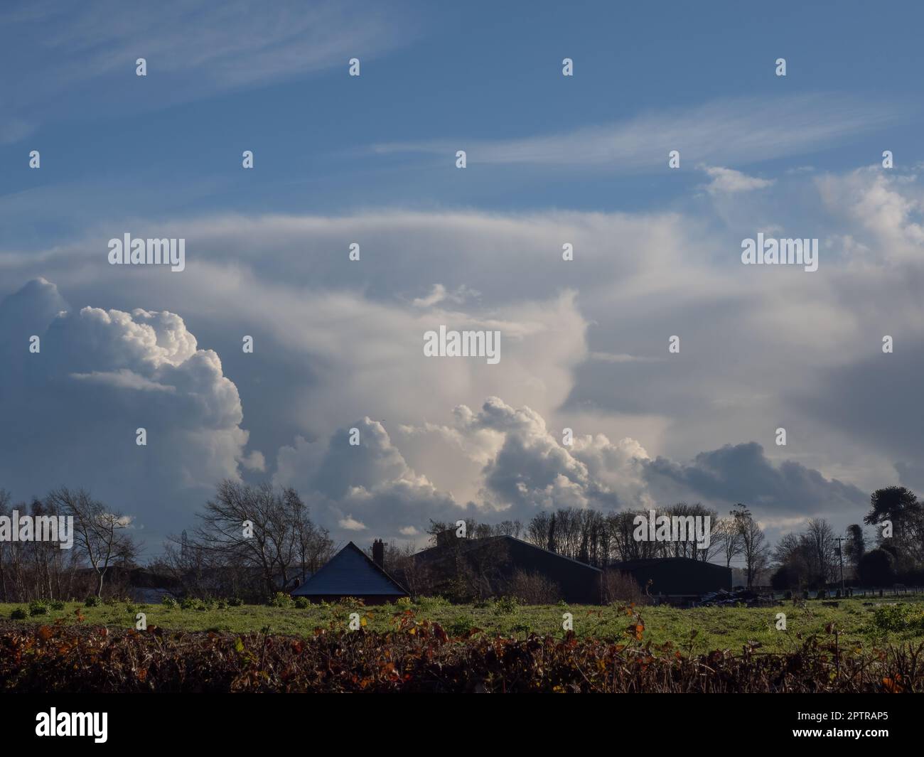 Dramatic clouds over Sussex on a Winter's late afternoon, with farm buildings and trees in foreground. Stock Photo