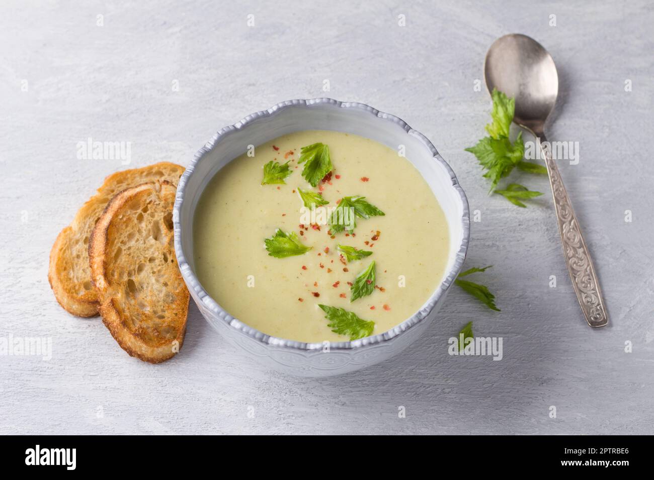 Cream soup of stalked celery with cream, garnished with celery leaves, pink pepper and served with crispy toast on a light gray background, top view Stock Photo