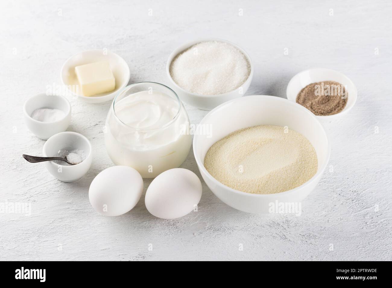 Ingredients for making a delicious semolina pie: semolina, eggs, sour cream or yogurt, sugar, vanilla sugar, butter, salt, soda on a light gray backgr Stock Photo