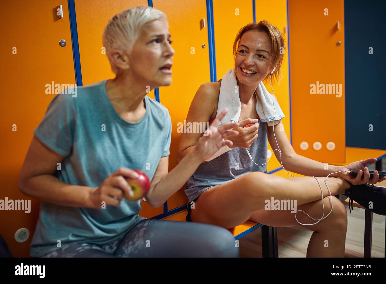 Senior woman and younger woman wearing sportswear having a joyful conversation in gym locker room. Stock Photo