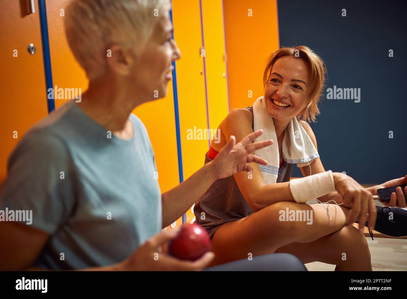 Young woman having a cheerful conversation with senior woman before training in gym locker room. Ready for workuot. Stock Photo