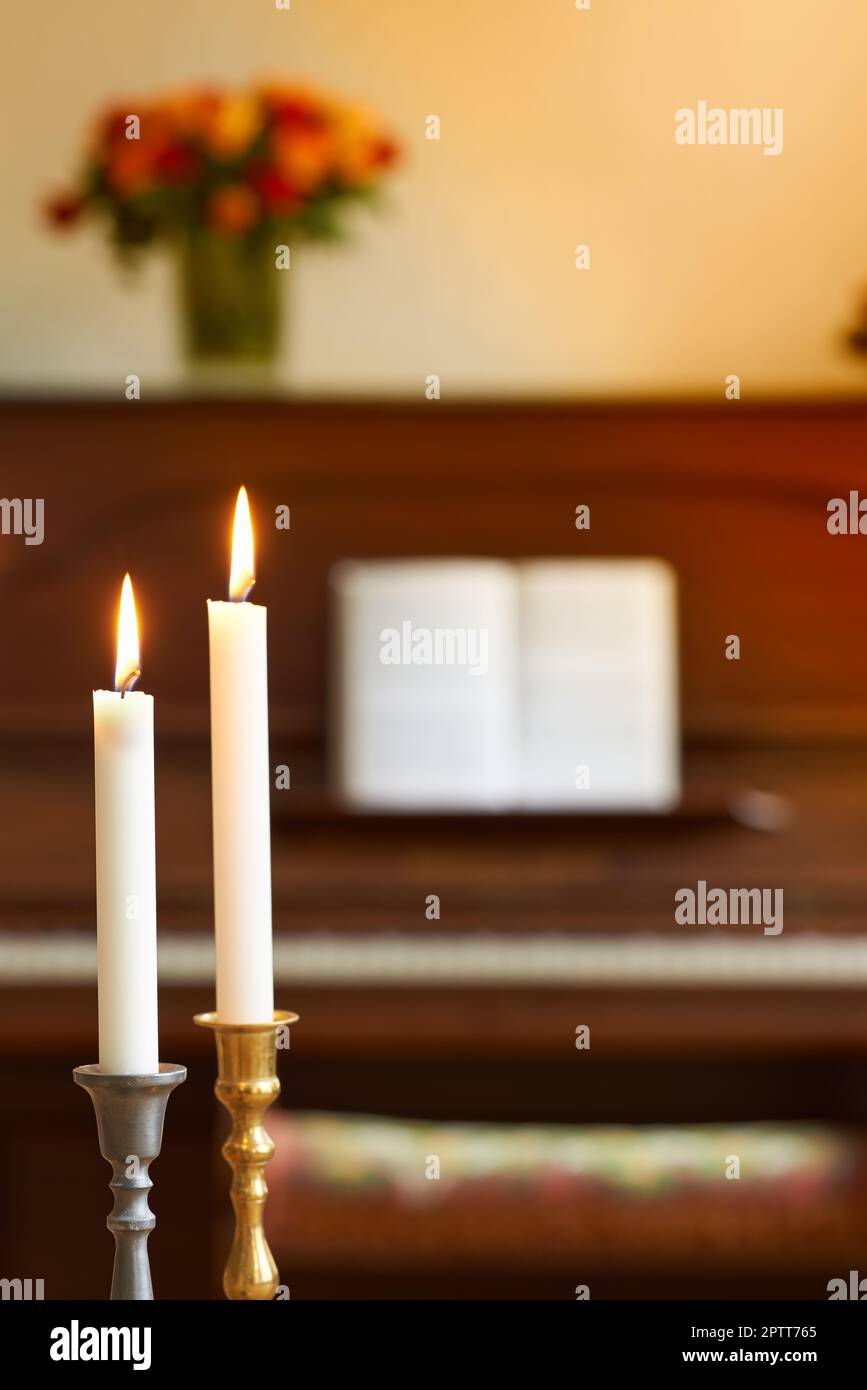 Two thin candles in candle stick holders burning against blurry piano