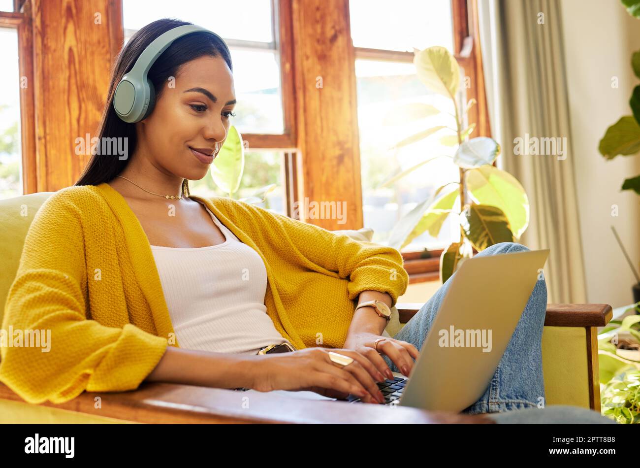 Hispanic woman typing on a laptop and listening to music on headphones ...