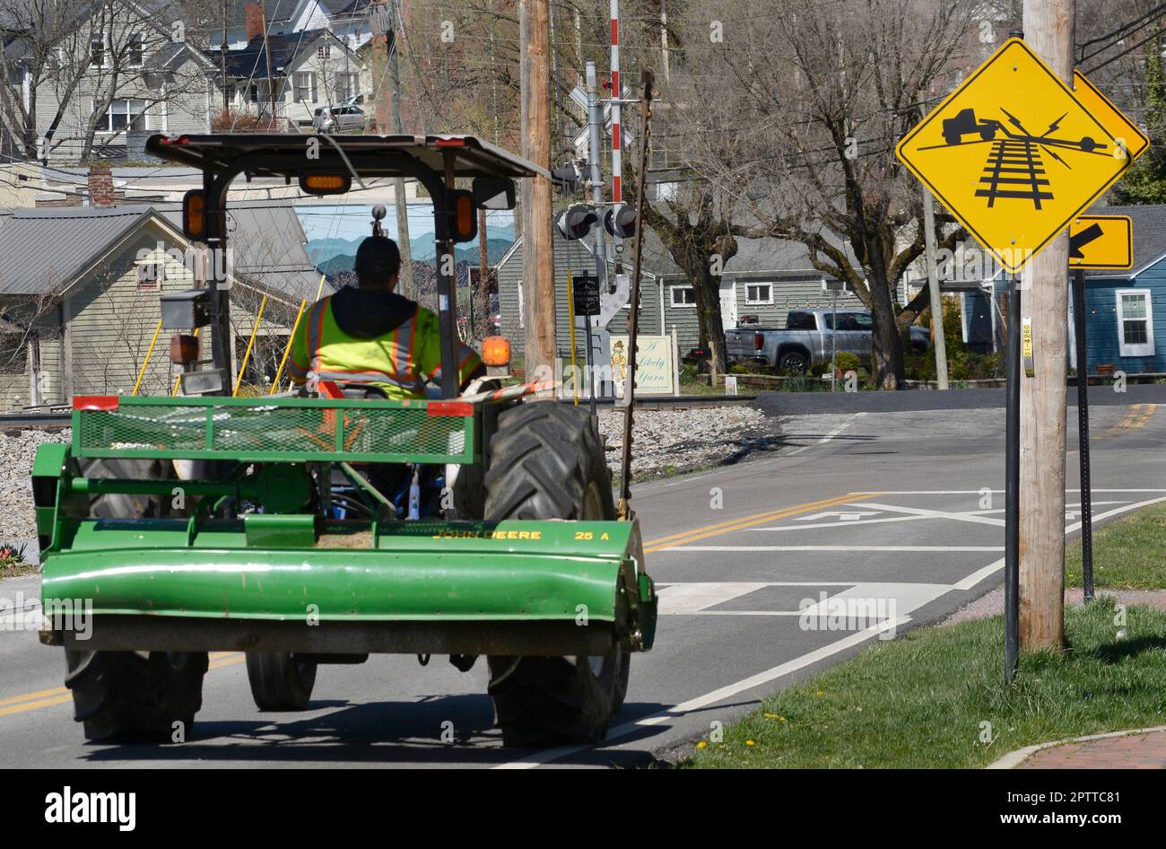 A worker drives a tractor equipped with a mowing blade and John Deere
