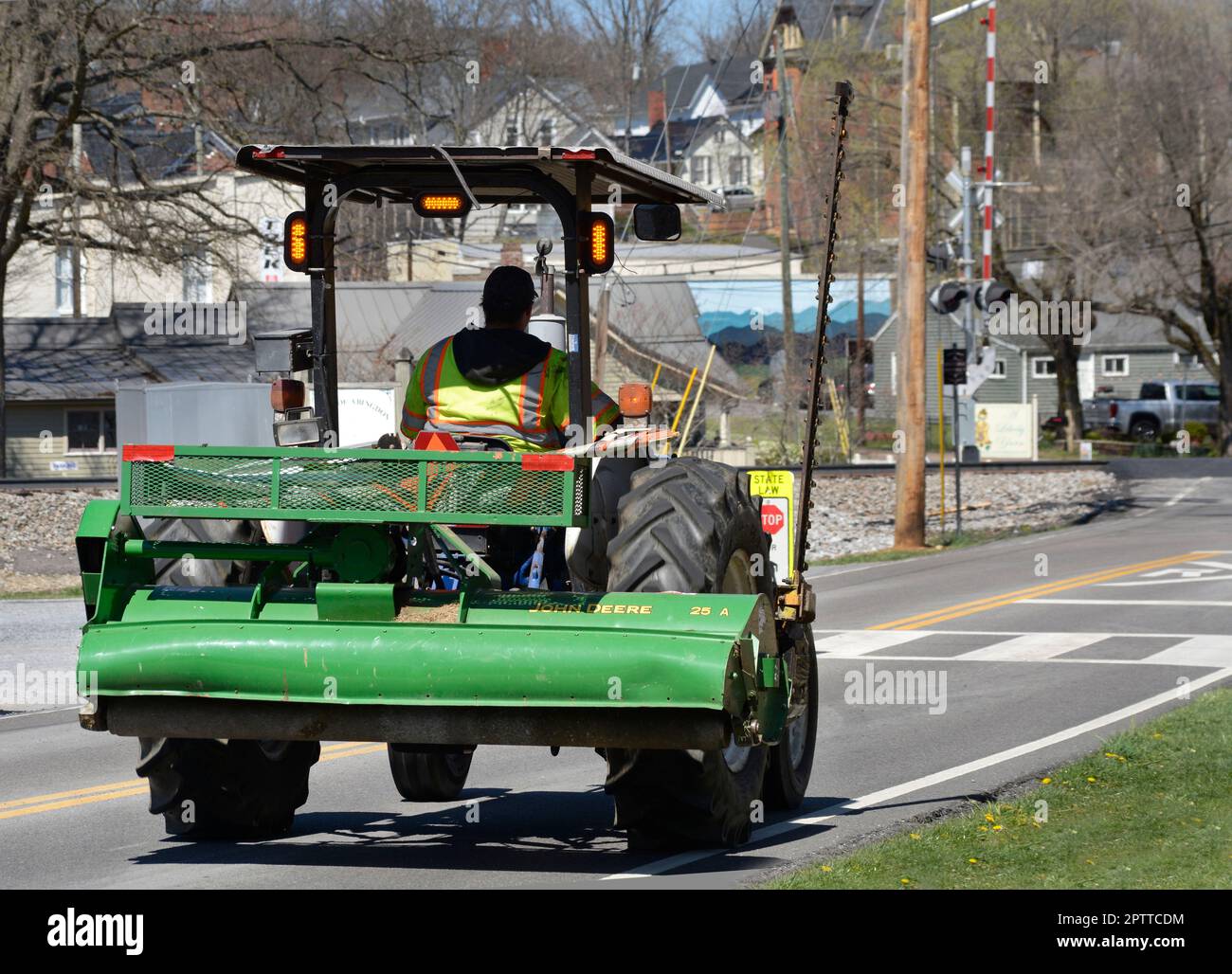 A worker drives a tractor equipped with a mowing blade and John Deere