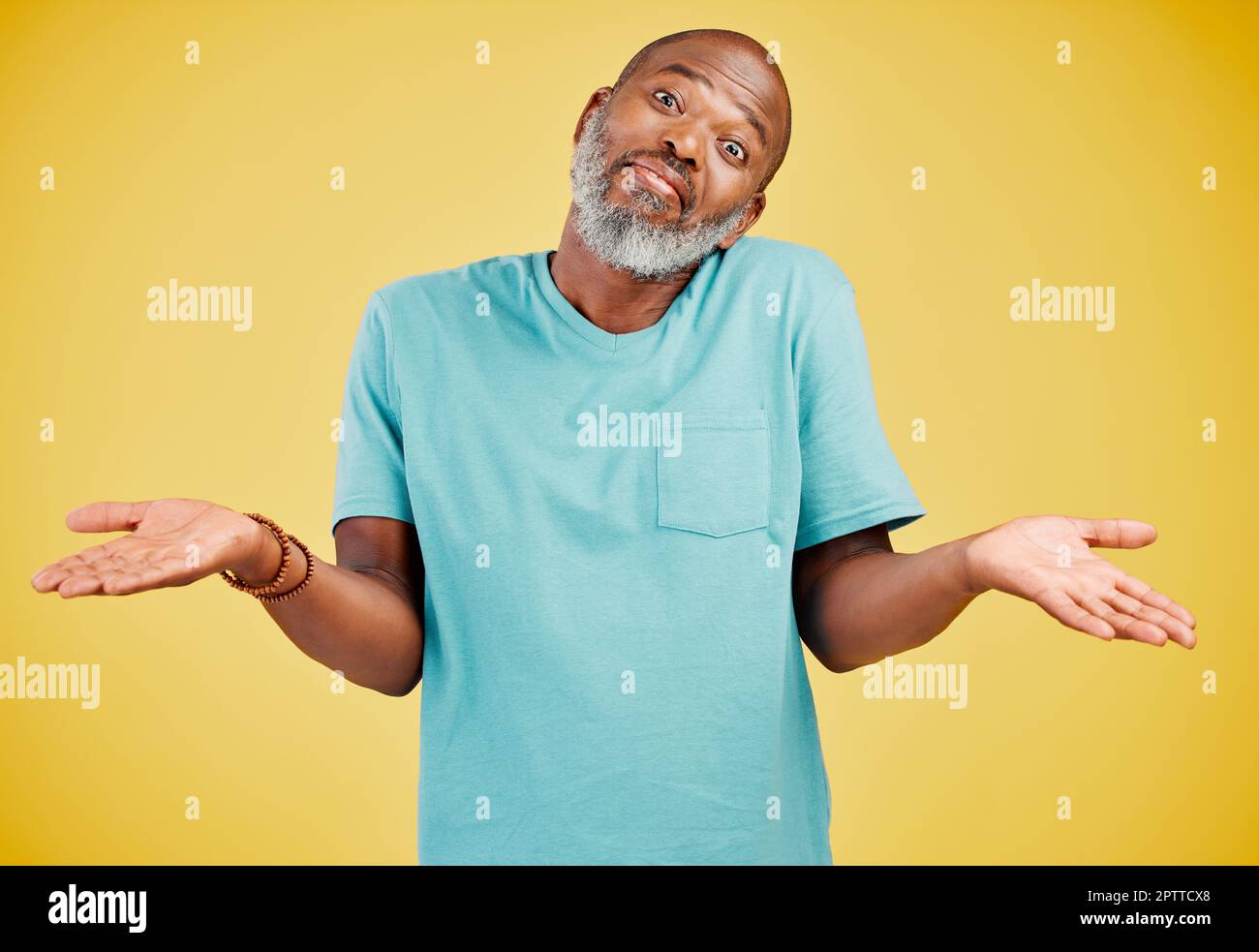 Portrait of a mature african american man smiling and making a gesture of not knowing something while smiling against a yellow studio background. Blac Stock Photo