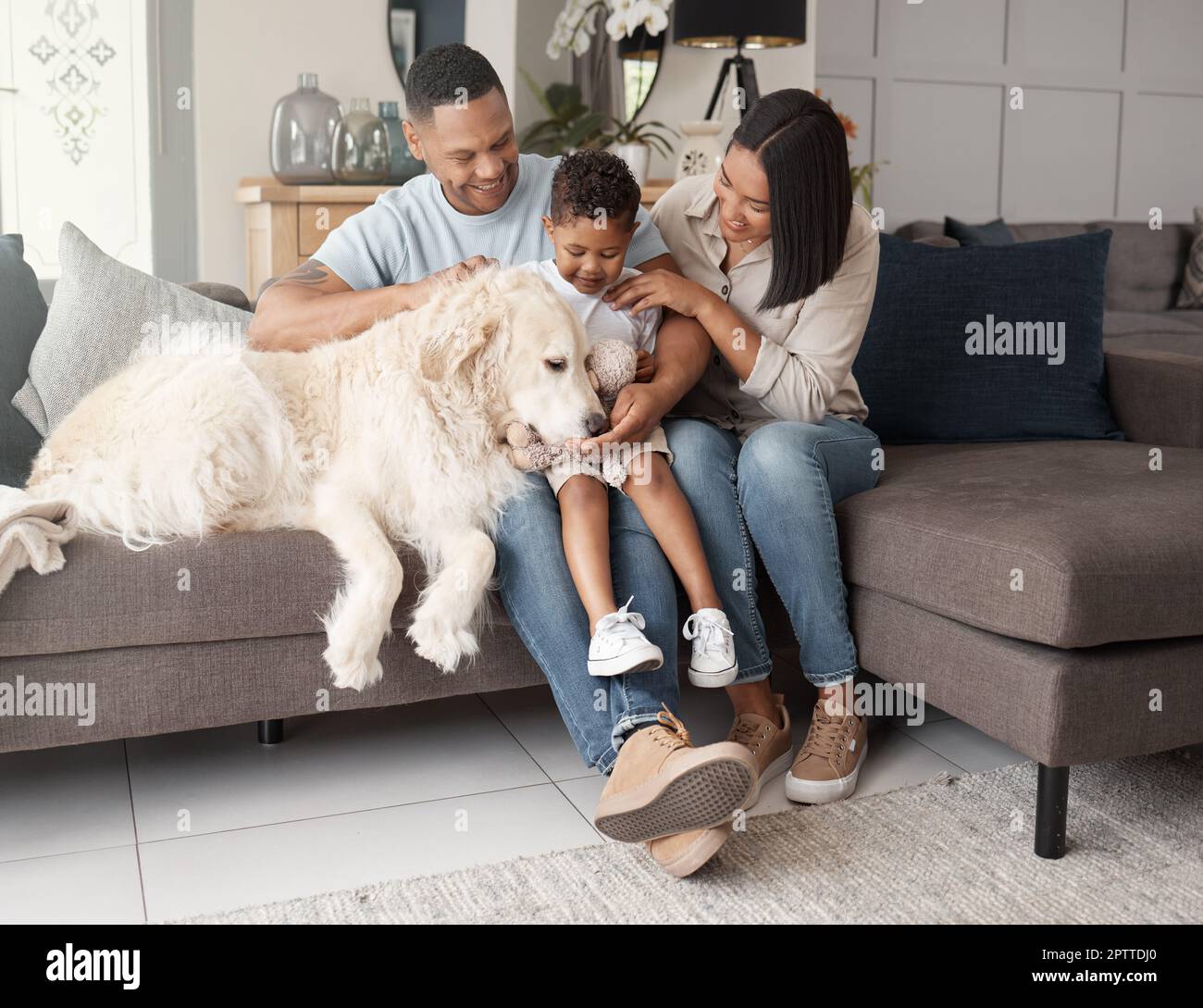 A happy mixed race family of three relaxing on the sofa with their dog. Loving black family being affectionate with a foster animal. Young couple bond Stock Photo