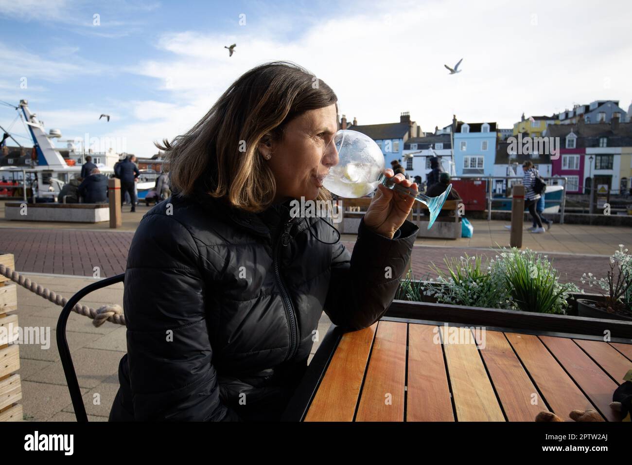 Woman drinking a gin and tonic whilst sitting outside a bar in the coastal town of Weymouth, Dorset, England Stock Photo