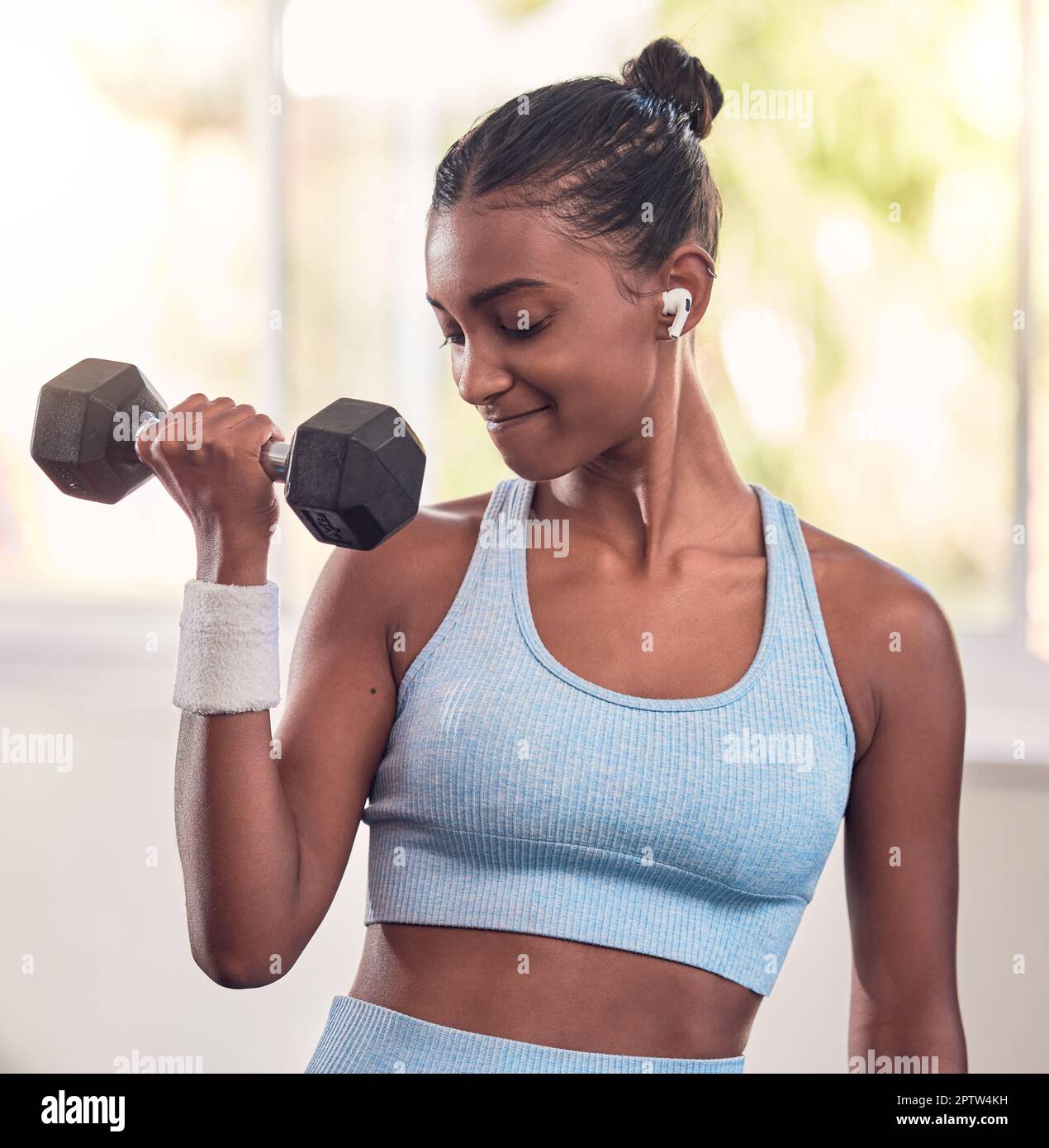Woman, dumbbell and music earphones in gym workout, training and exercise for strong arm muscles, body goals or strength target. Indian athlete, perso Stock Photo