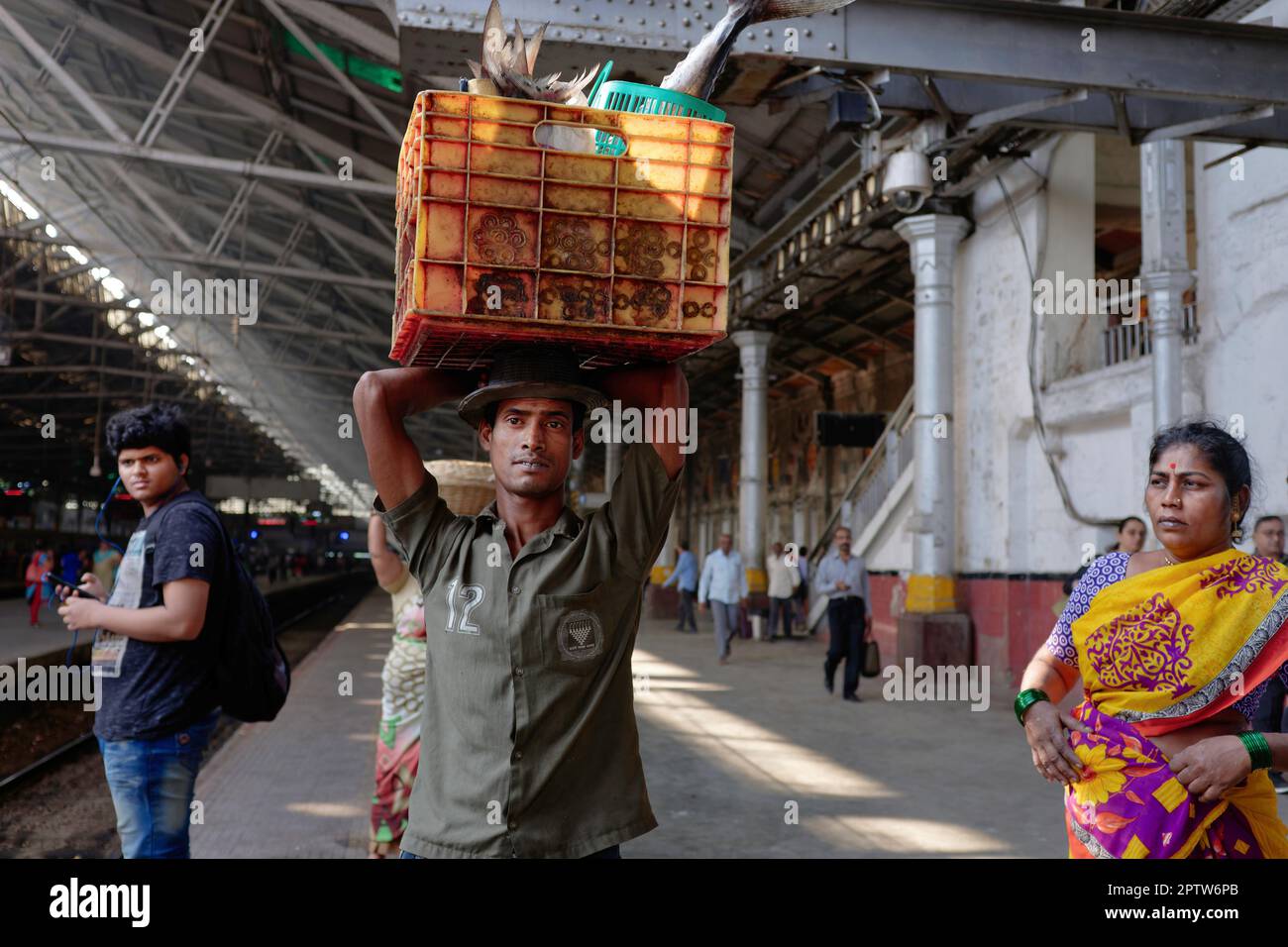 A porter at Chhatrapati Shivaji Maharaj Terminus in Mumbai, India, waiting for a local train to forward his crate of fish Stock Photo