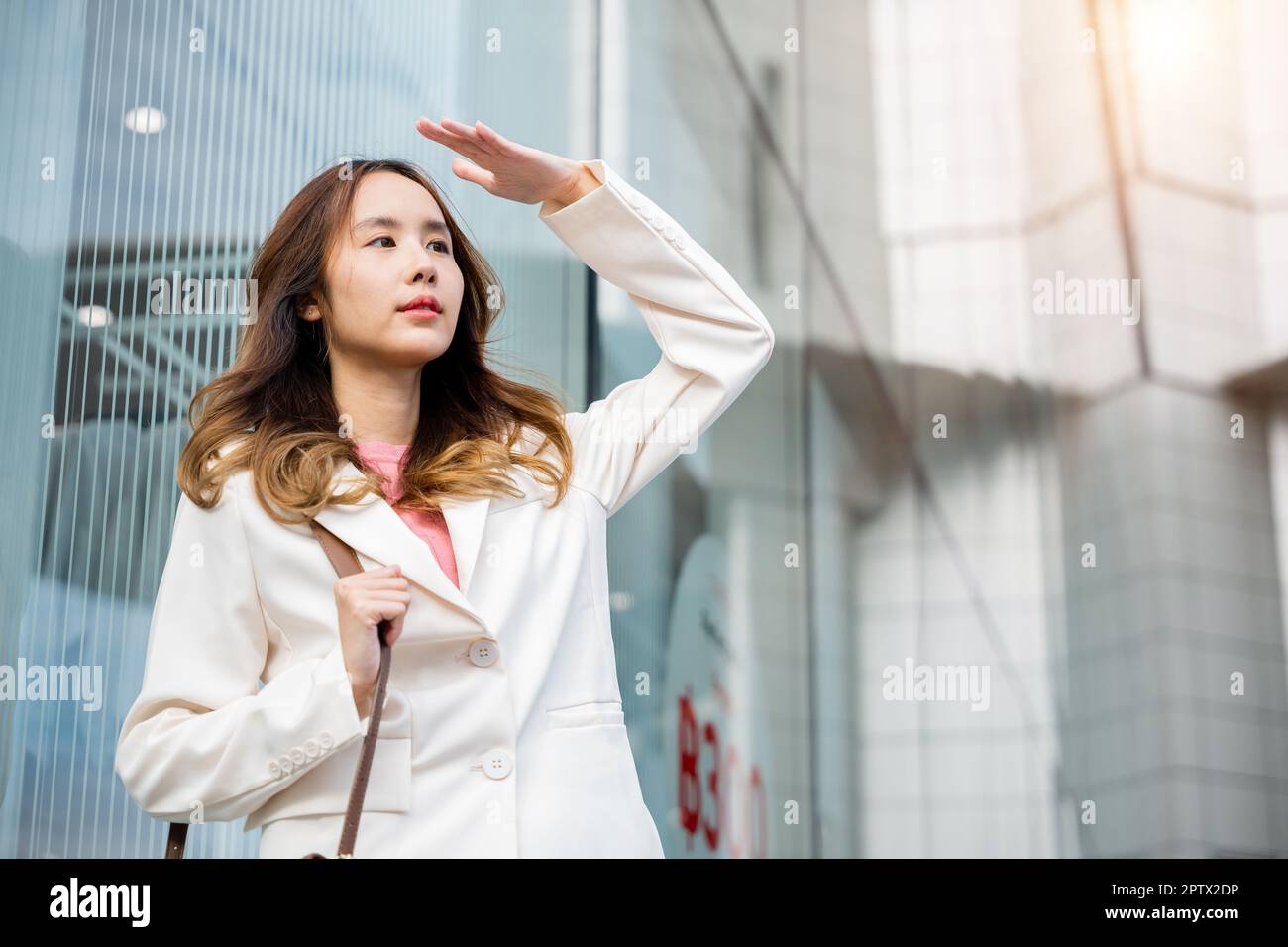 Portrait of confidence young businesswoman standing outside office building  in city raise your hand to shade the sun. Happy woman wearing white suit j  Stock Photo - Alamy