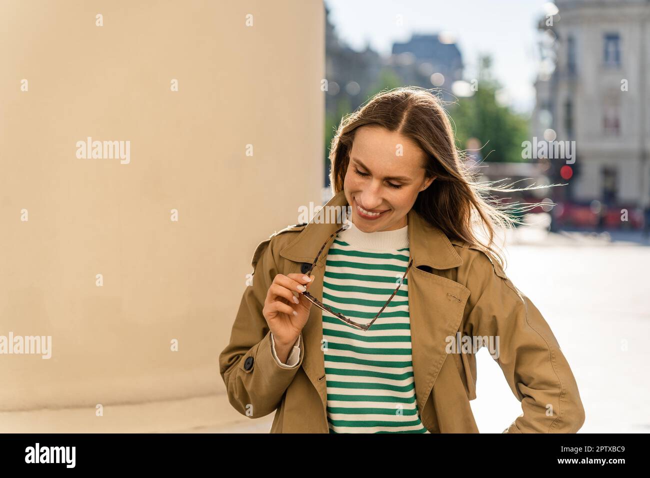 A woman smiles and holds sunglasses while walking in the city Stock Photo