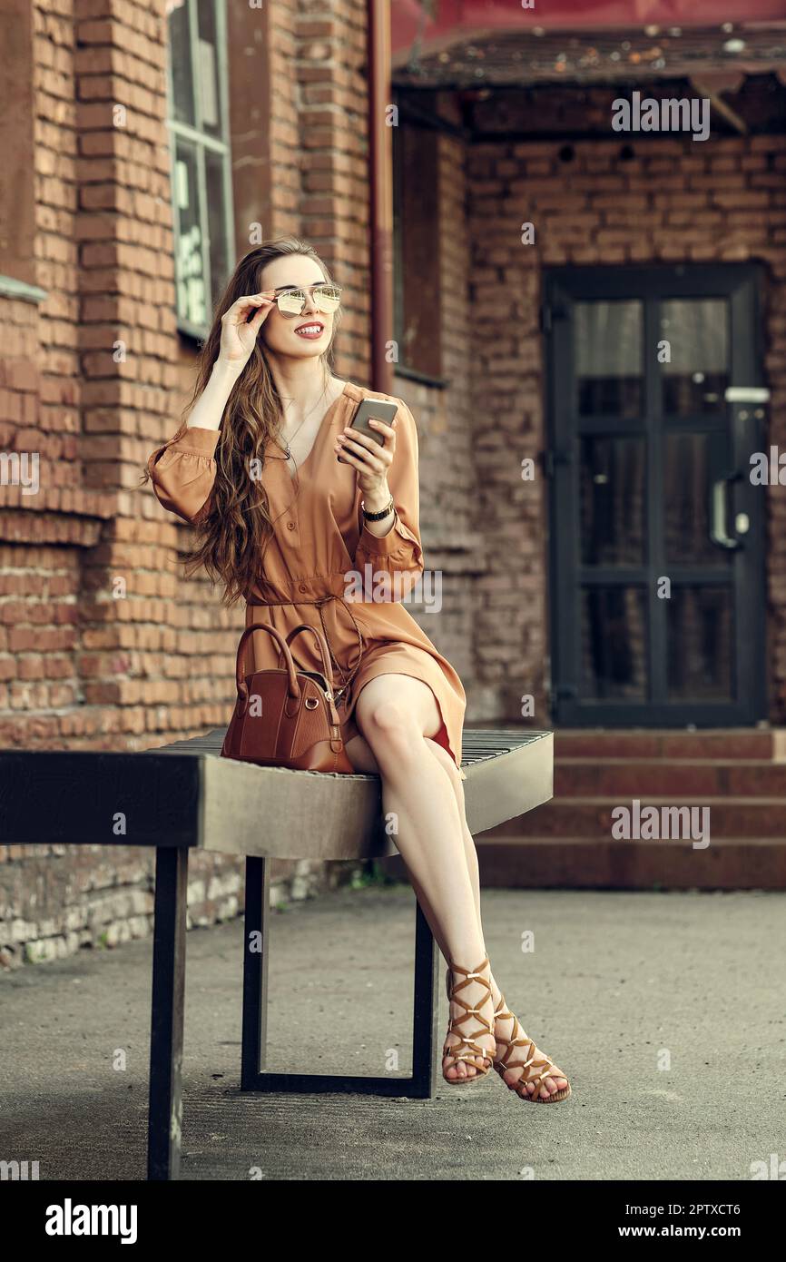 Cute girl in short dress sitting on bench with smartphone in hand Stock Photo - Alamy Cute girl in short dress sitting on bench with smartphone in hand Stock Photo - Alamy