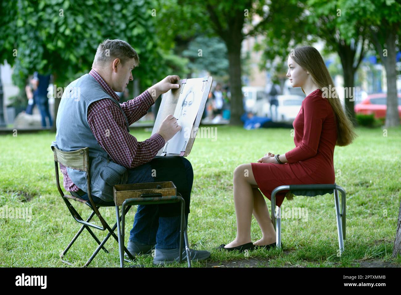 Painting in a park. Painter drawing girl sitting in front of him. May