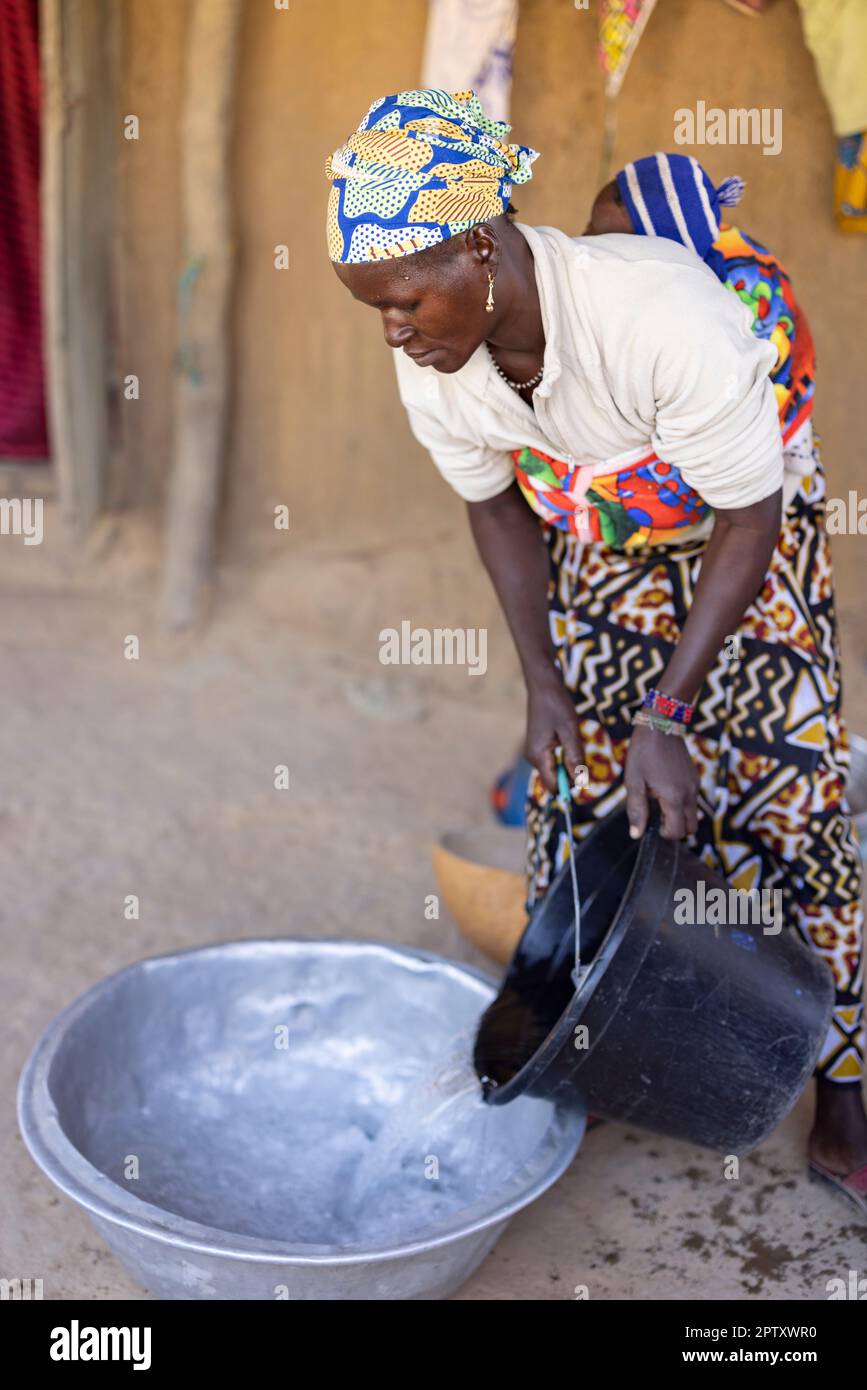 A mother washes clothes at her home while carrying her newborn baby on her back in Segou Region, Mali, West Africa. 2022 Mali drought and hunger crisis. Stock Photo