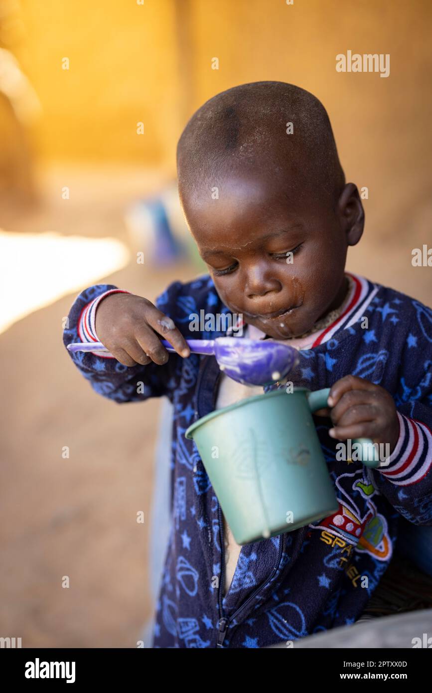 A hungry young child eats a meal of millet porridge from a cup in Segou Region, Mali, West Africa. 2022 Mali drought and hunger crisis. Stock Photo