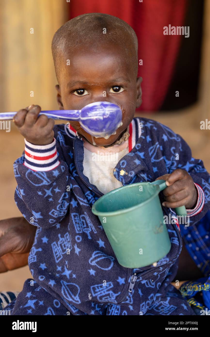 A hungry young child eats a meal of millet porridge from a cup in Segou Region, Mali, West Africa. 2022 Mali drought and hunger crisis. Stock Photo