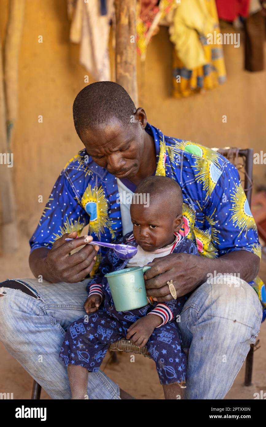 An African father spoonfeeds his son a breakfast meal of millet ...