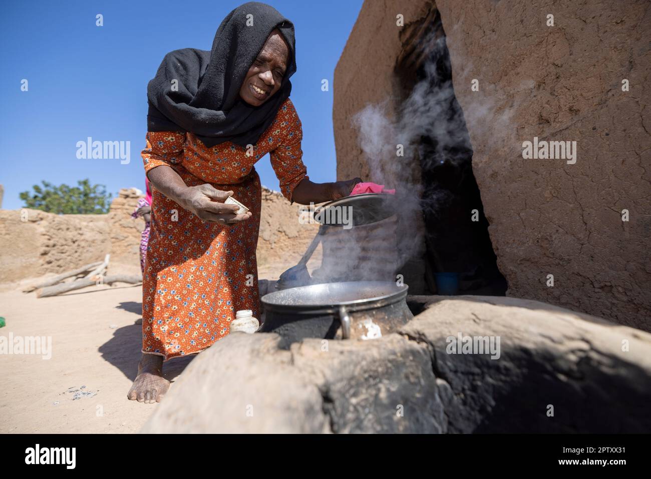 An elderly woman cooks over an earthen homemade stove outside her house in Segou Region, Mali, West Africa. 2022 Mali drought and hunger crisis. Stock Photo