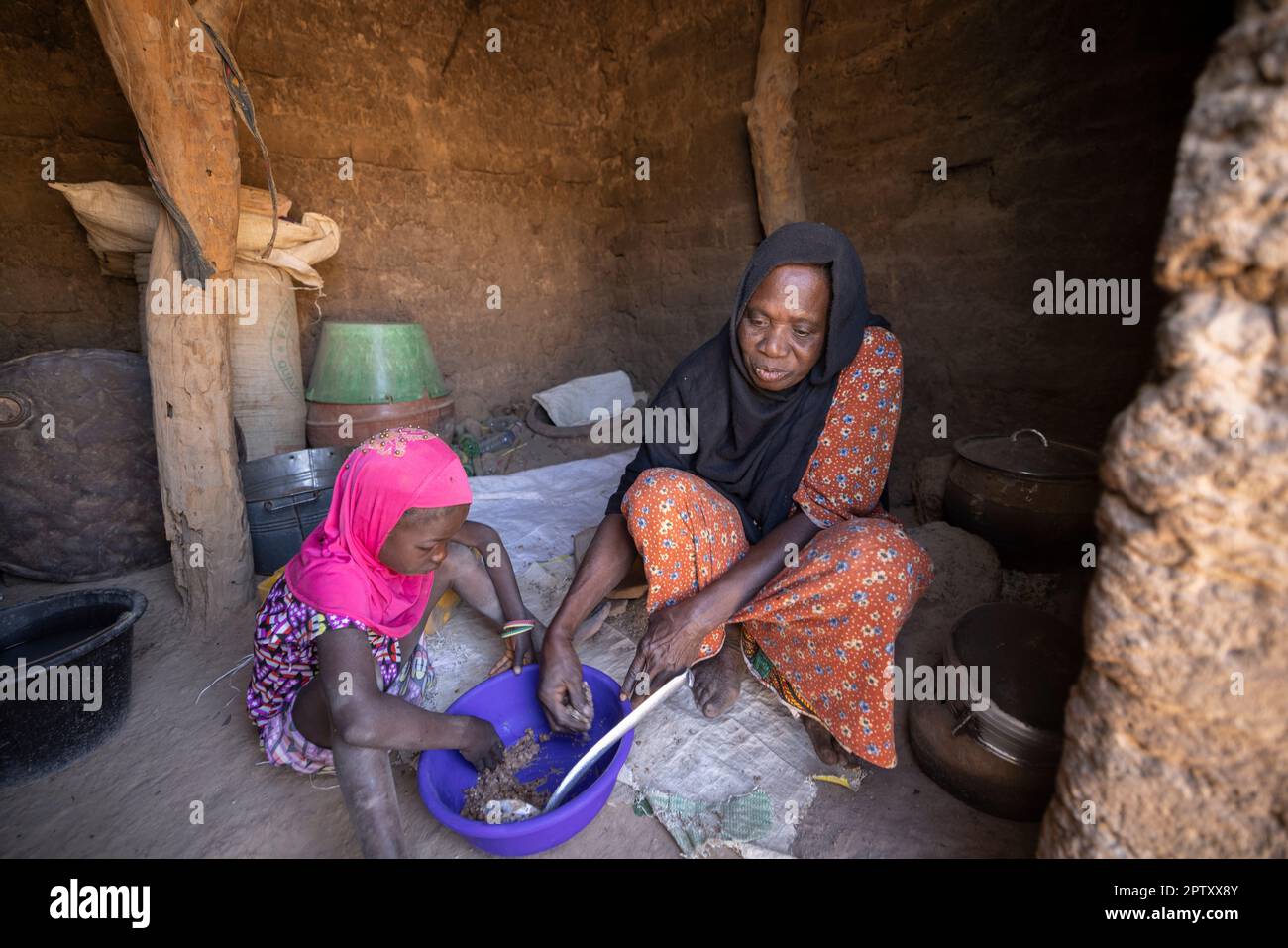 A young child and her grandmother eat a meager meal on the floor of  their home in Segou Region, Mali, West Africa. 2022 Mali drought and hunger crisis. Stock Photo