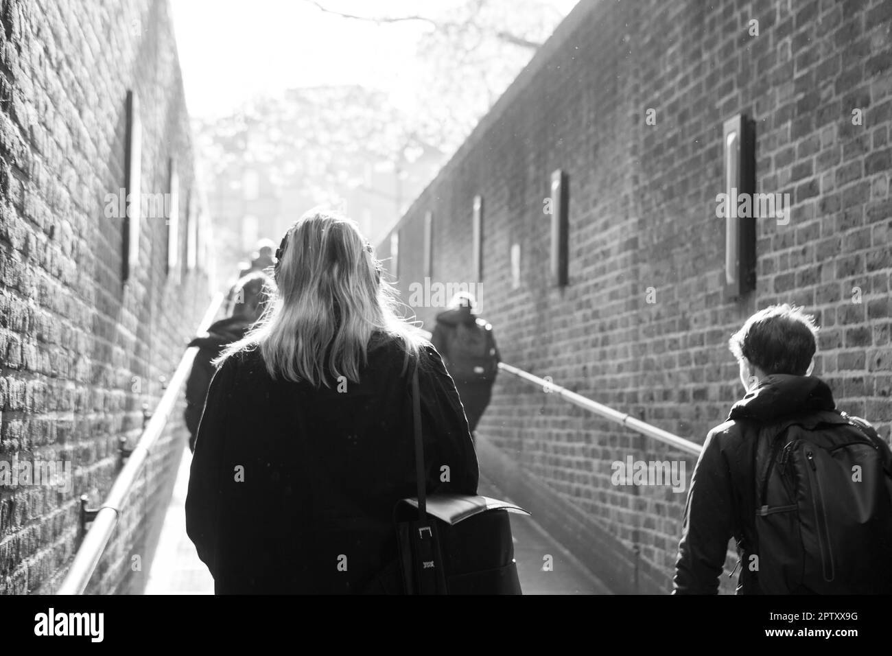 London, UK, 25 April 2023: At Pimlico tube station people walk up the ramp to exit the station on their way to work or school. Sunshine beams down on them and spring leaves on a tree can be seen in the distance. Anna Watson/Alamy Stock Photo