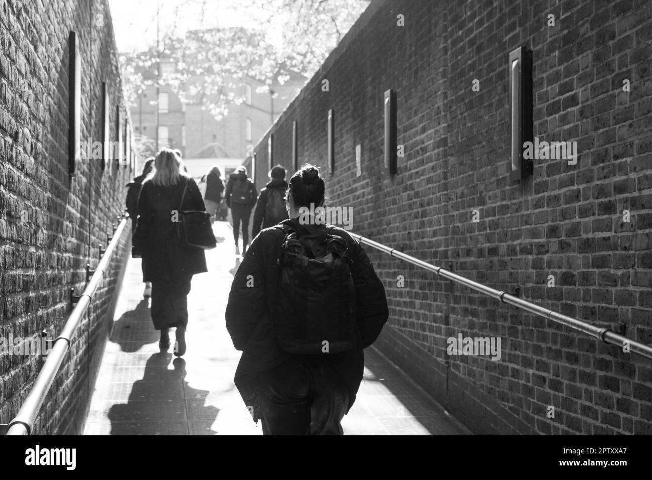London, UK, 25 April 2023: At Pimlico tube station people walk up the ramp to exit the station on their way to work. Sunshine beams down on them and spring leaves on a tree can be seen in the distance. Anna Watson/Alamy Stock Photo