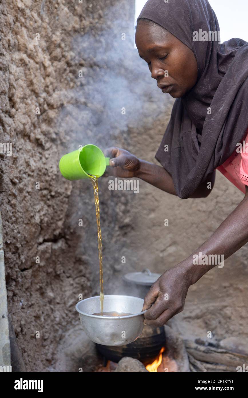 A African woman pours a freshly boiled serving of tea at her home in Segou Region, Mali, West Africa. 2022 Mali drought and hunger crisis. Stock Photo