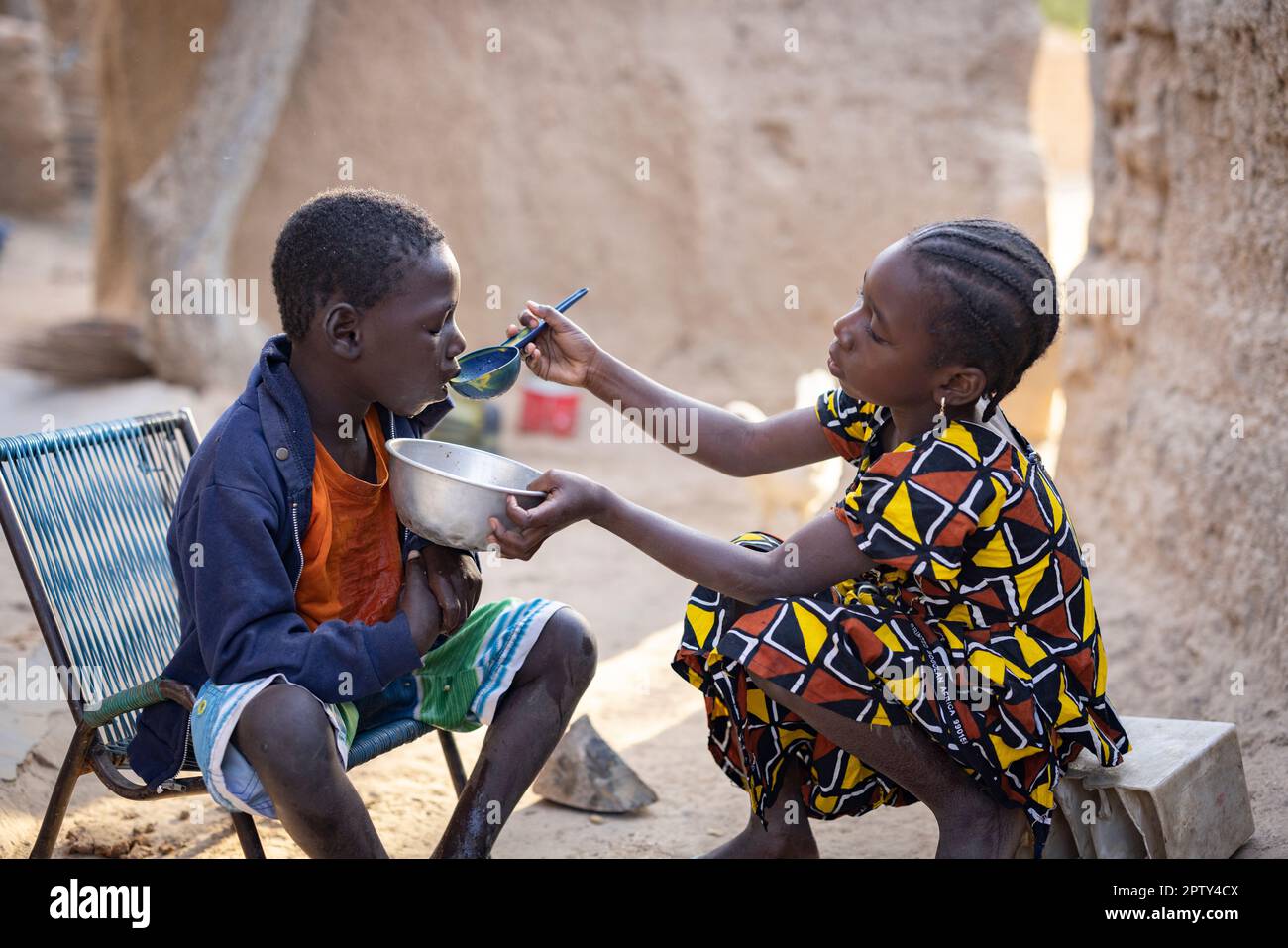 A young girl feeds her disabled brother at their home in Segou Region, Mali, West Africa. 2022 Mali drought and hunger crisis. Stock Photo