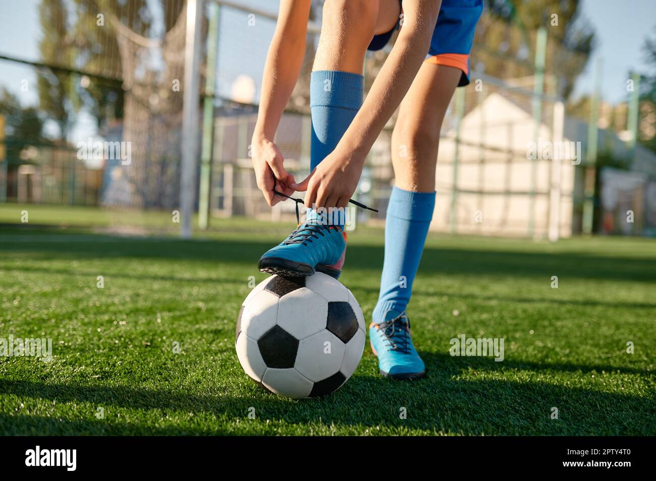 Closeup little football player tying shoelaces putting leg on soccer
